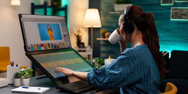 Woman with editor occupation wearing headphones at studio office desk. Professional graphic artist working on picture editing background for template using touchpad monitor screen